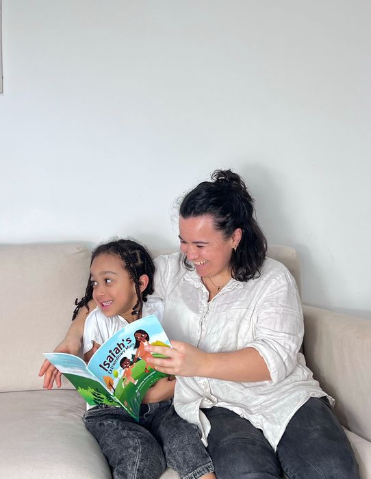 A parent and child sitting on a sofa reading a Little Omo picture book together