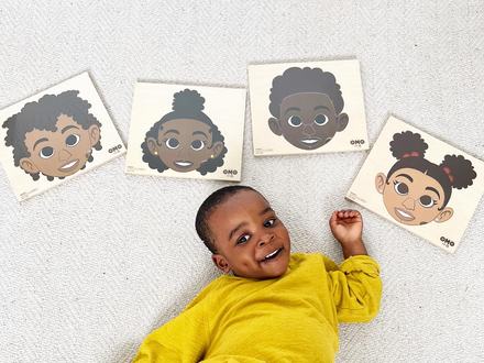 A toddler lying beside four wooden face puzzles